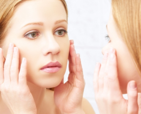 A beautiful girl examining her face in the mirror to check for any acne presence.